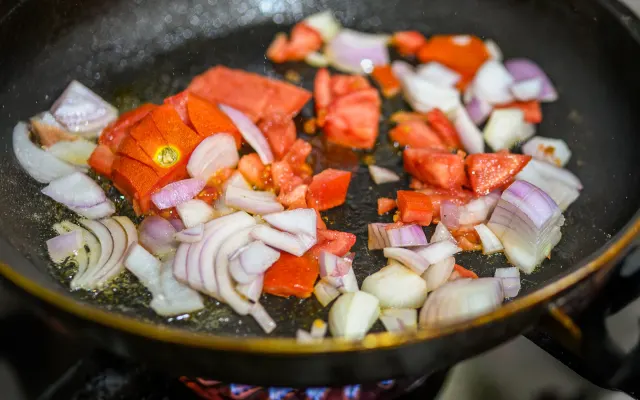 Chopped onions and tomatoes softening in a pan on a gas stove