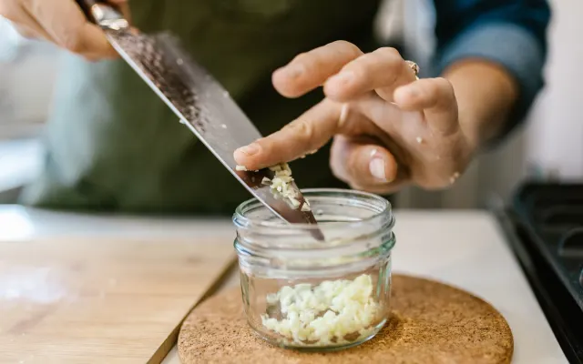 Chopped garlic being spooned into a glass storage jar