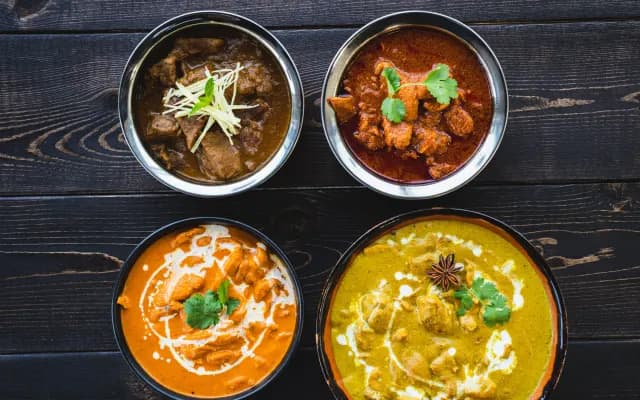 Four Indian dishes in steel bowls on a dark wooden table