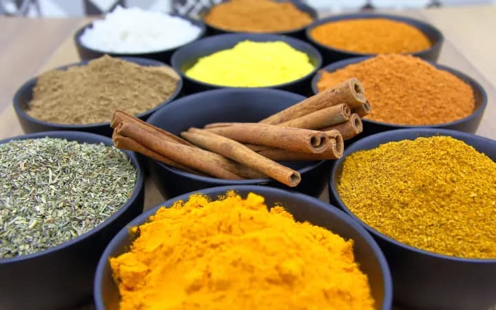 Ground spices in separate bowls with whole cinnamon sticks between them